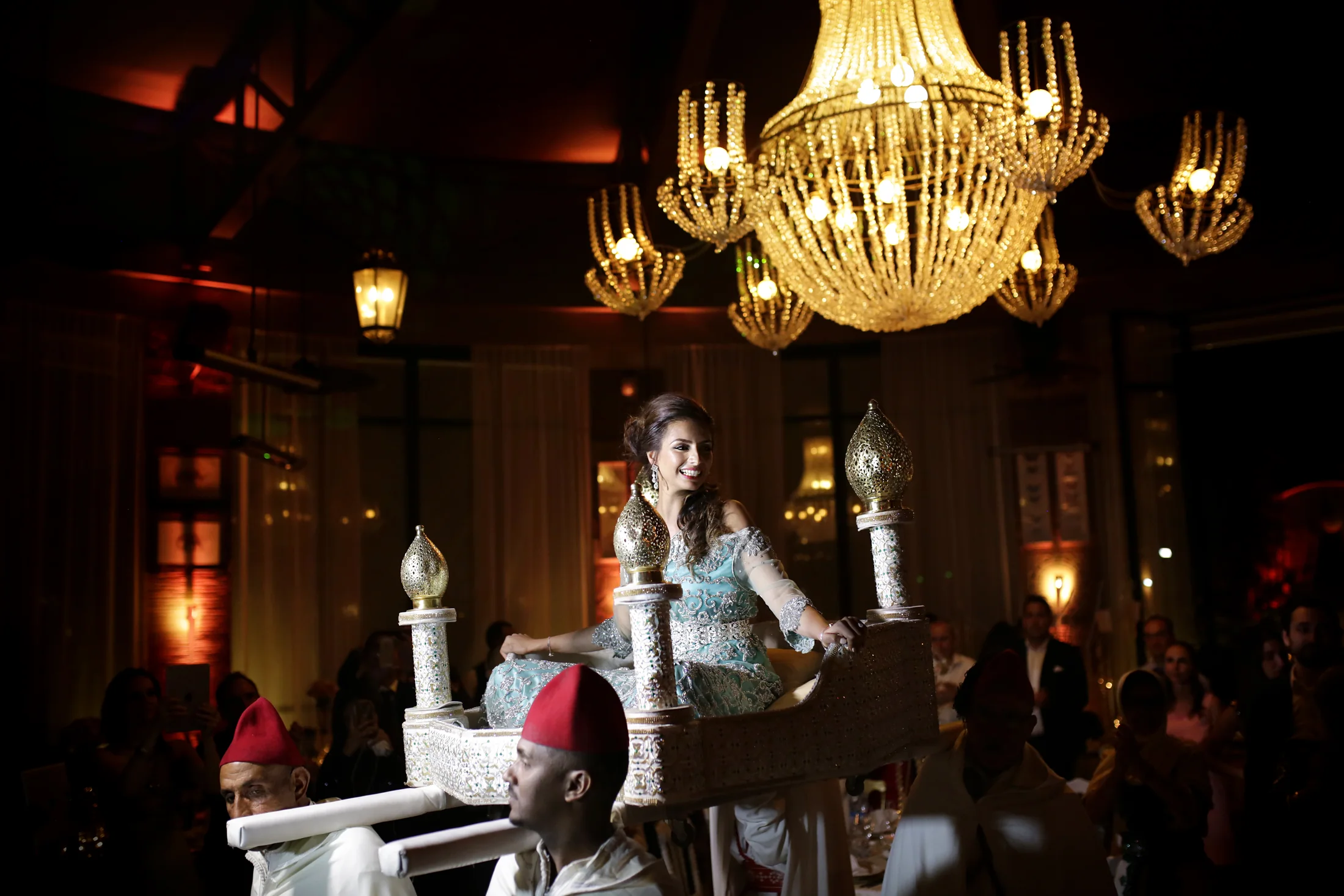A bride carried beneath chandeliers during an evening celebration