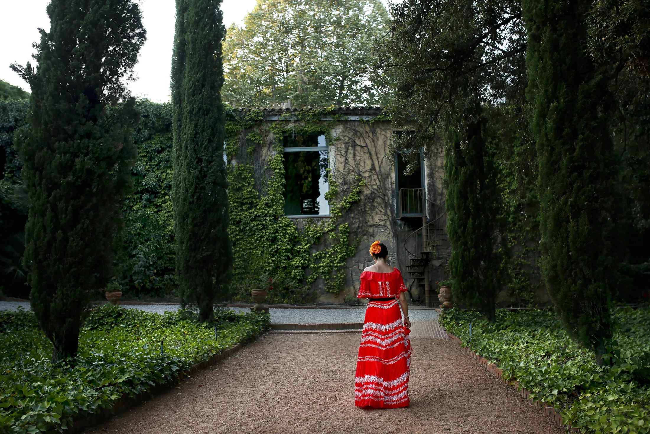 A figure in vivid red walking through a formal garden